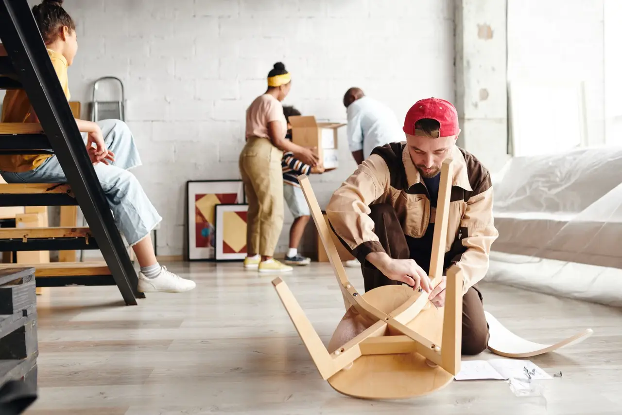 Group of people assembling furniture in a spacious room, with a focus on a man adjusting a chair, emphasizing professional montage services in Vienna by Kraftpack.